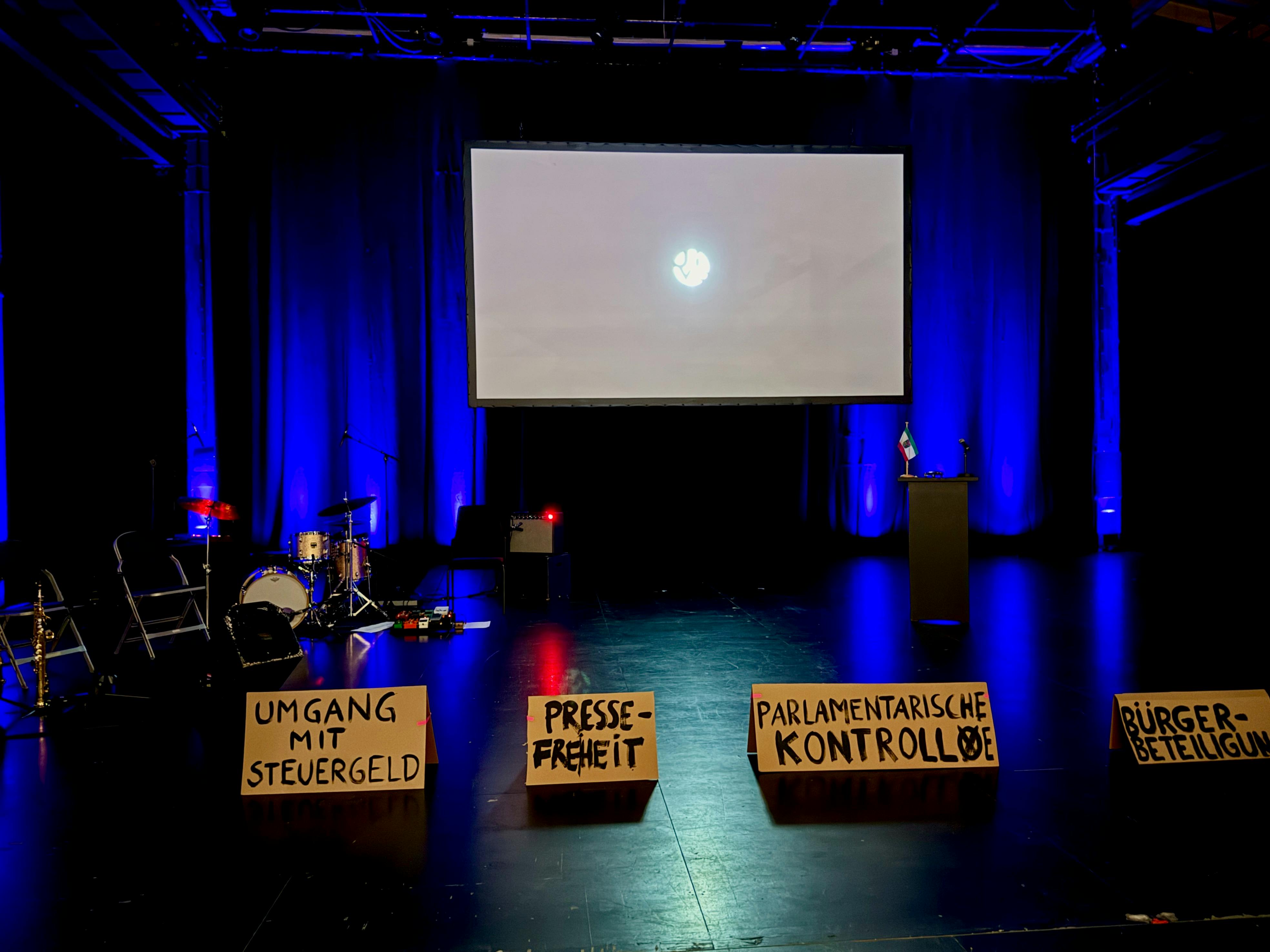 Die JIVE-Bühne kurz vor dem Start mit den Instrumenten der Band, einer Leinwand  und Pappschildern mit Beschriftungen.