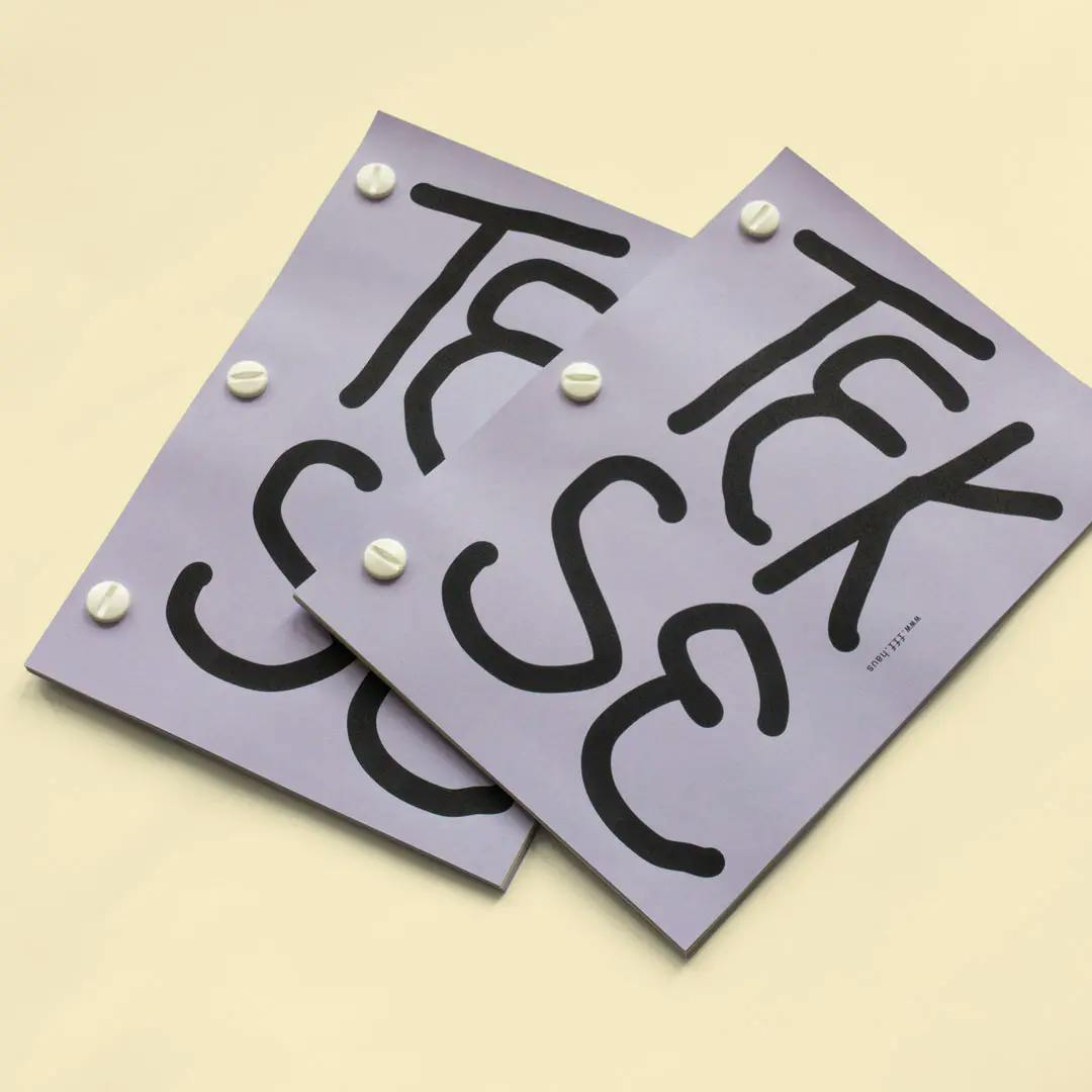 Two overlapping purple booklets with large black letters spelling 'TEKSE'