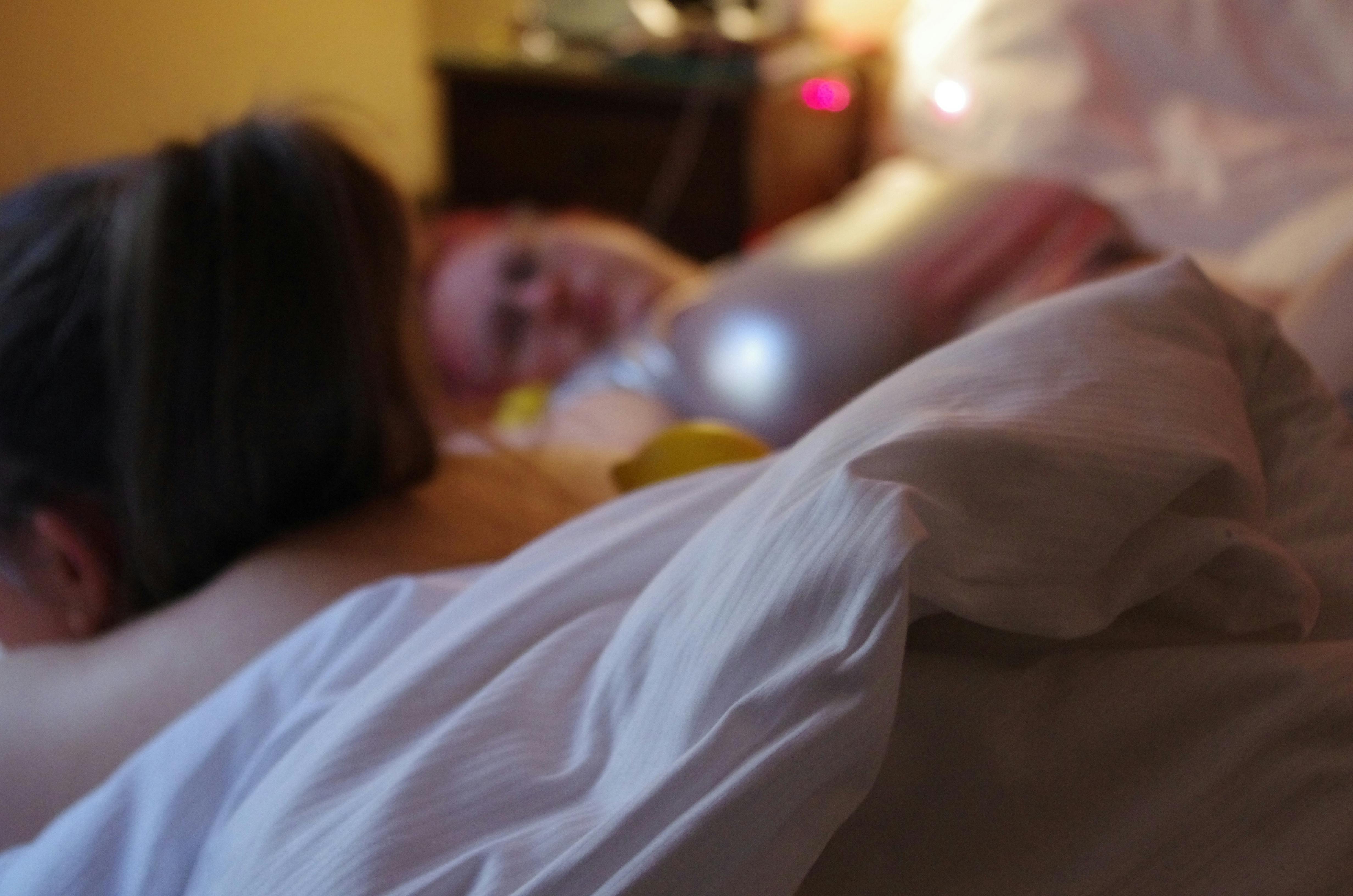 Foto von Julianna in einem Hotelbett. Es ist ein weißes Leintuch zu sehen, Annas Hinterkopf mit Pferdeschwanz und Julias verschwommenes Gesicht und silbernes Shirt.