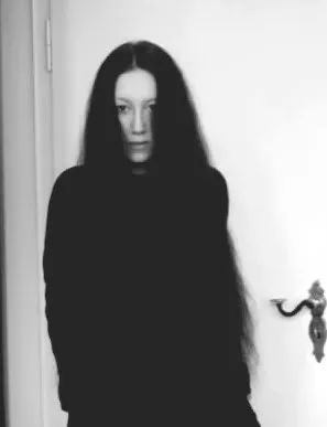 Schwarz weißes Bild von mir vor einer weißen Tür. Ich trage schwarz, die Haare sind offen und lang.