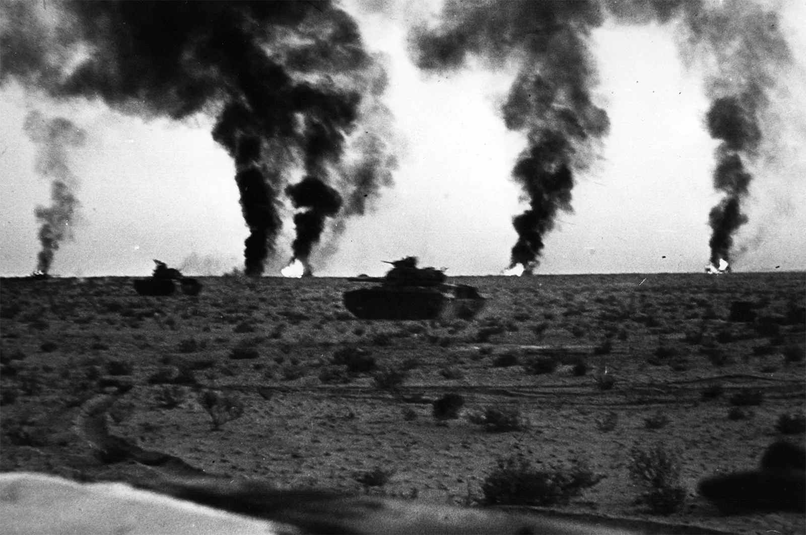 Zwei israelische Panzer in der Wüste, im Hintergrund fünf Rauchsäulen brennender Panzer.