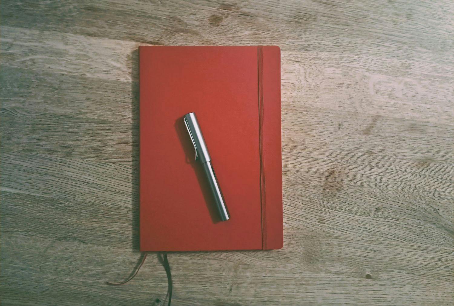 Rotes Notizbuch liegt auf einem Tisch, darauf ein silberner Füller.