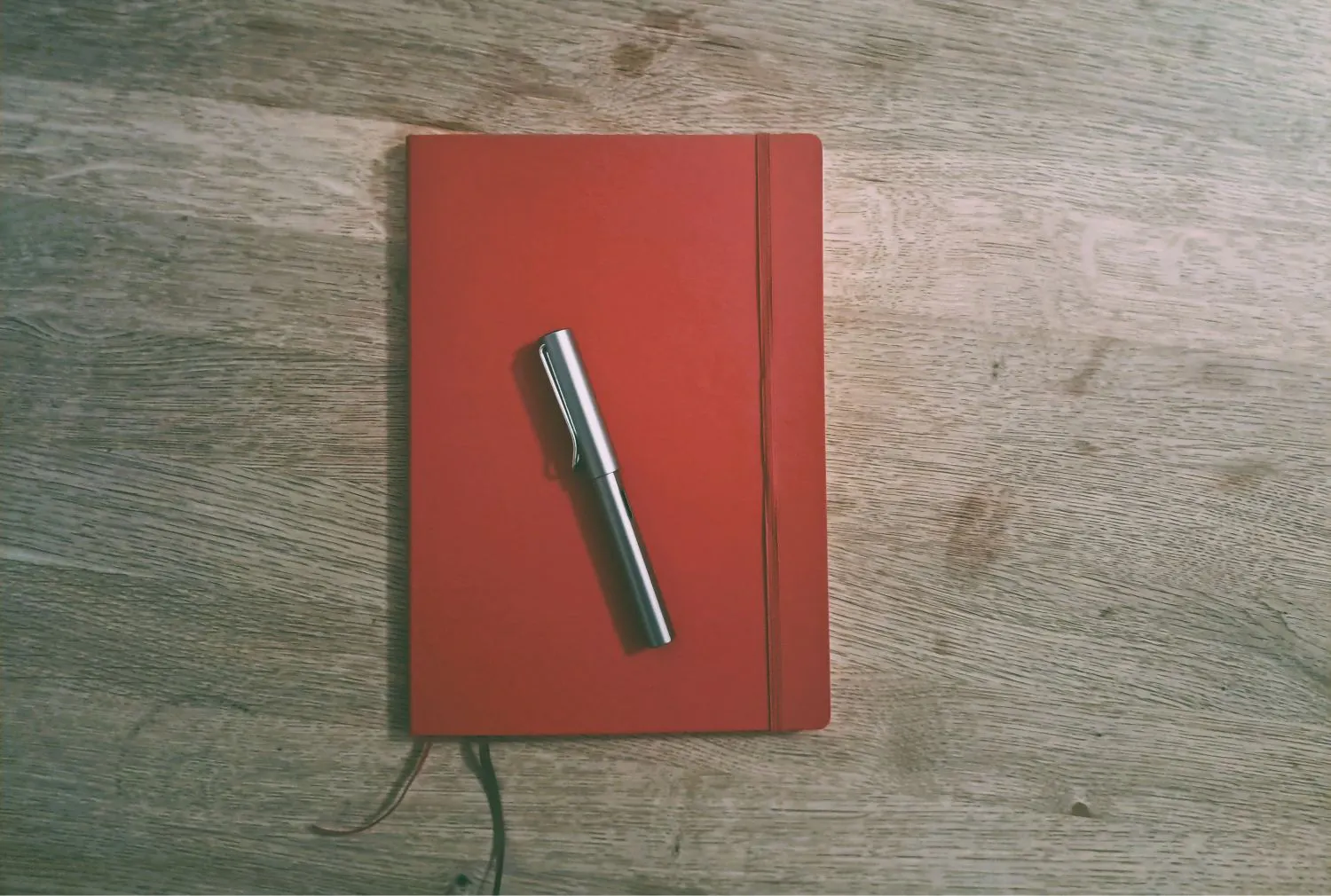 Rotes Notizbuch liegt auf einem Tisch, darauf ein silberner Füller.