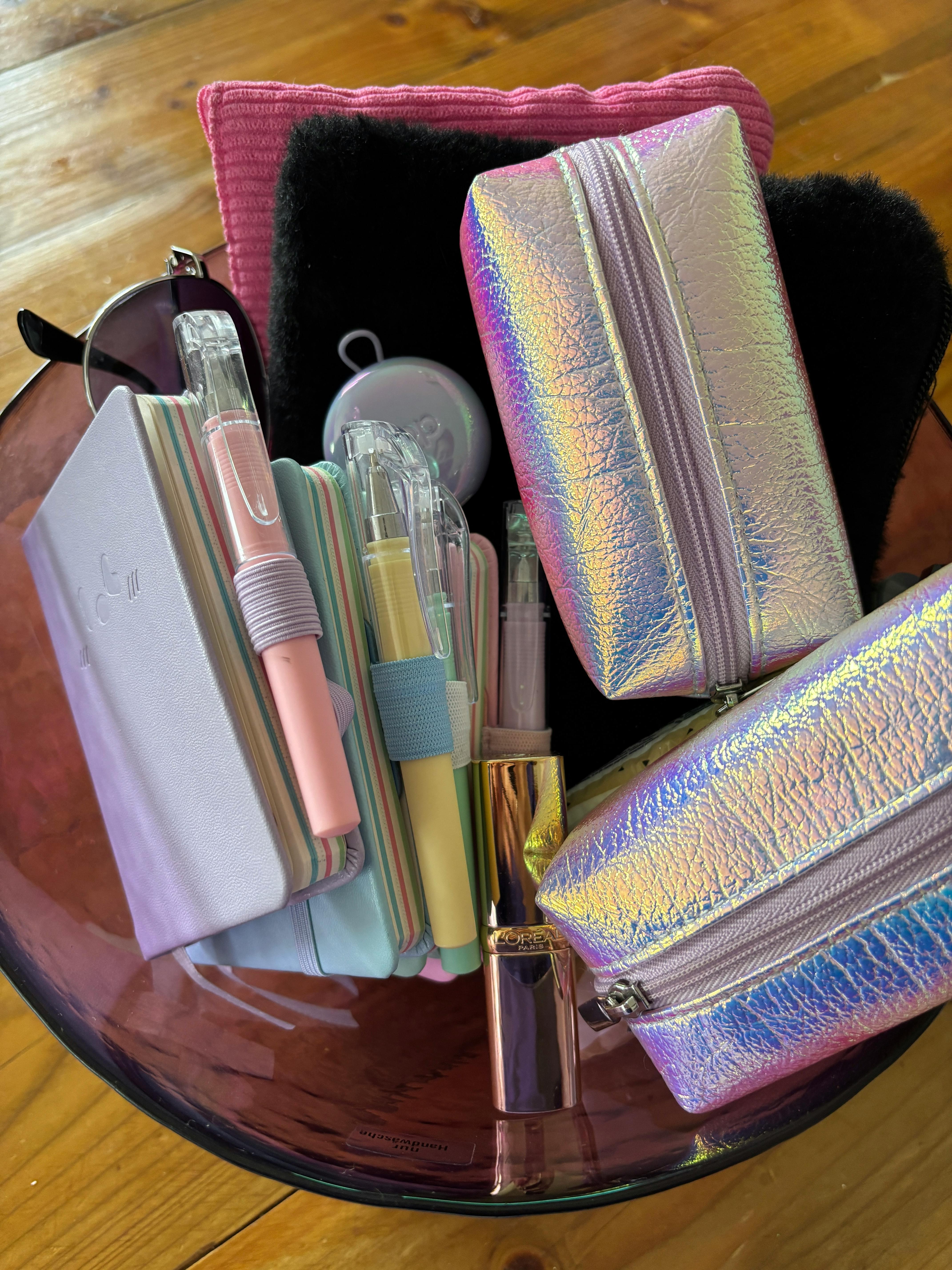 Lila Schüssel mit Lippenstift, Sonnenbrille, Notizbuch, Ohrstöpseln und Visitenkartenmäppchen und Etuis