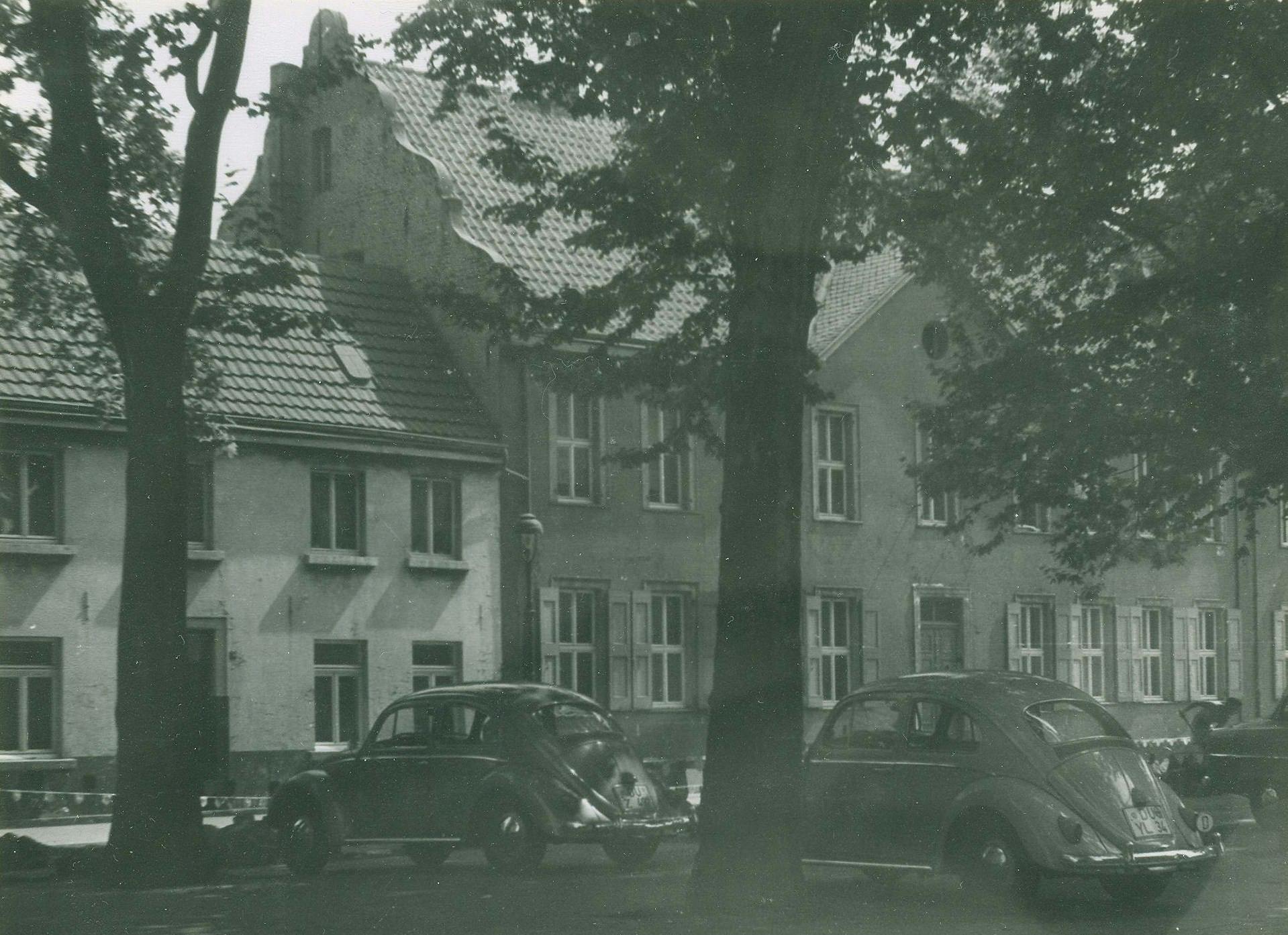 Foto des Neumarktes in Duisburg-Ruhrort. Blick auf die ehemalige Zentrale Haniel ein zweigeschossiger Bau mit geschweiftem Treppengiebel, im Vordergrund parken mehrere VW-Käfer (Foto: Stadtarchiv Duisburg).