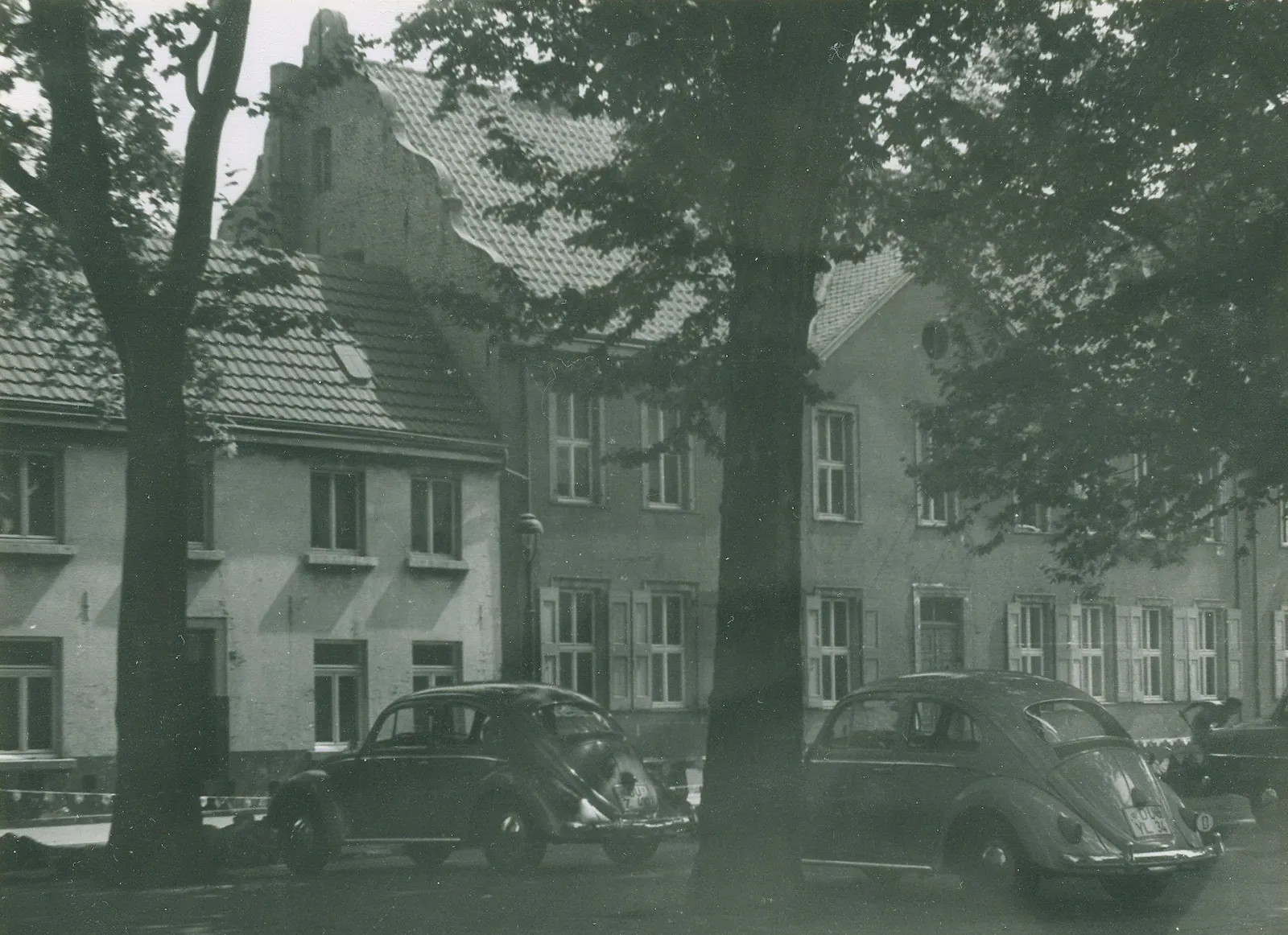 Foto des Neumarktes in Duisburg-Ruhrort. Blick auf die ehemalige Zentrale Haniel ein zweigeschossiger Bau mit geschweiftem Treppengiebel, im Vordergrund parken mehrere VW-Käfer (Foto: Stadtarchiv Duisburg).