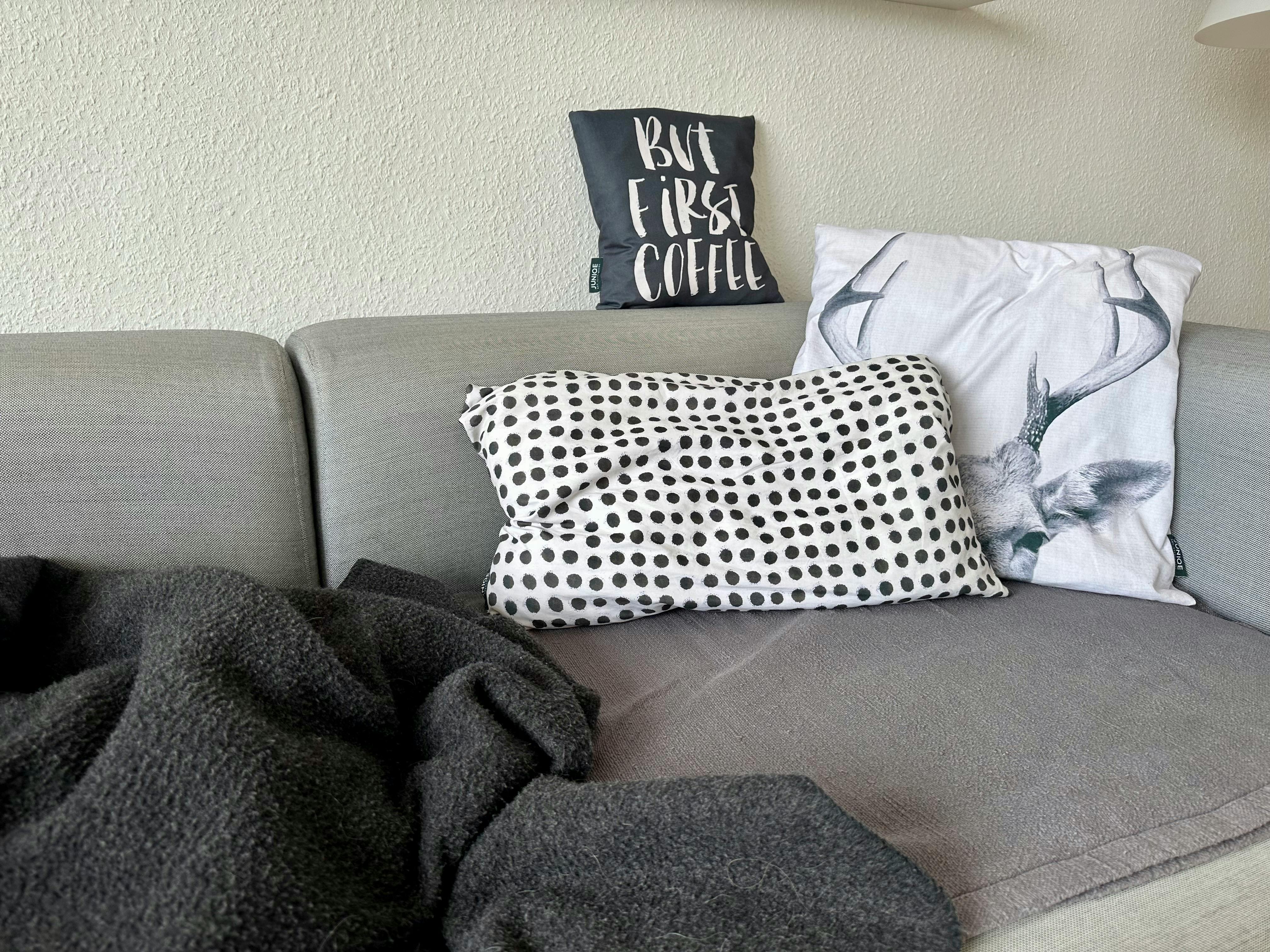 Graue Couch mit schwarz-weißen Kissen und einer anthrazith-farbenen Wolldecke darauf