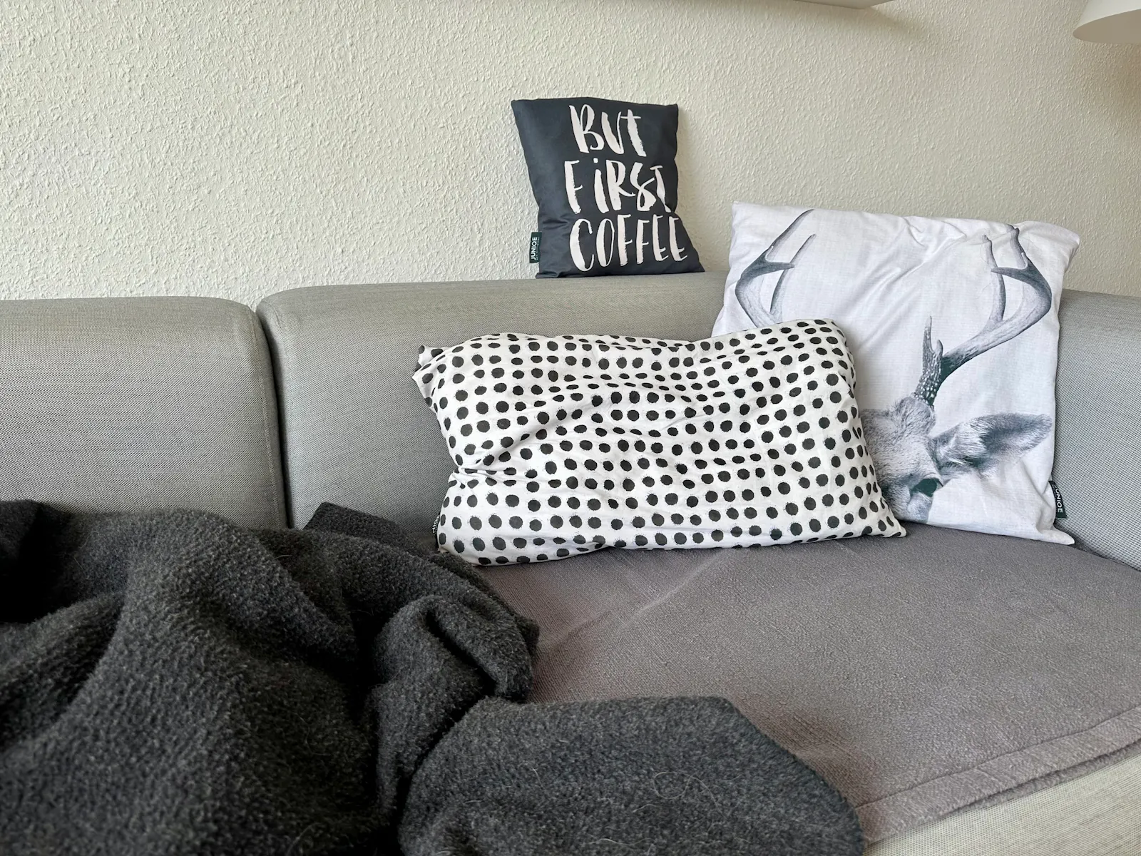 Graue Couch mit schwarz-weißen Kissen und einer anthrazith-farbenen Wolldecke darauf