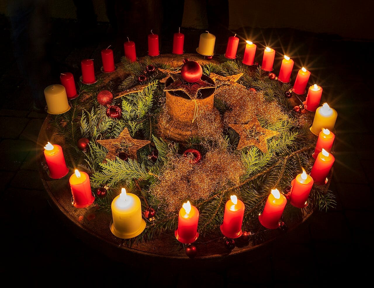 Ein Adventskranz mit 20 roten und 4 weißen Kerzen. Einige von ihnen sind schon angesteckt.