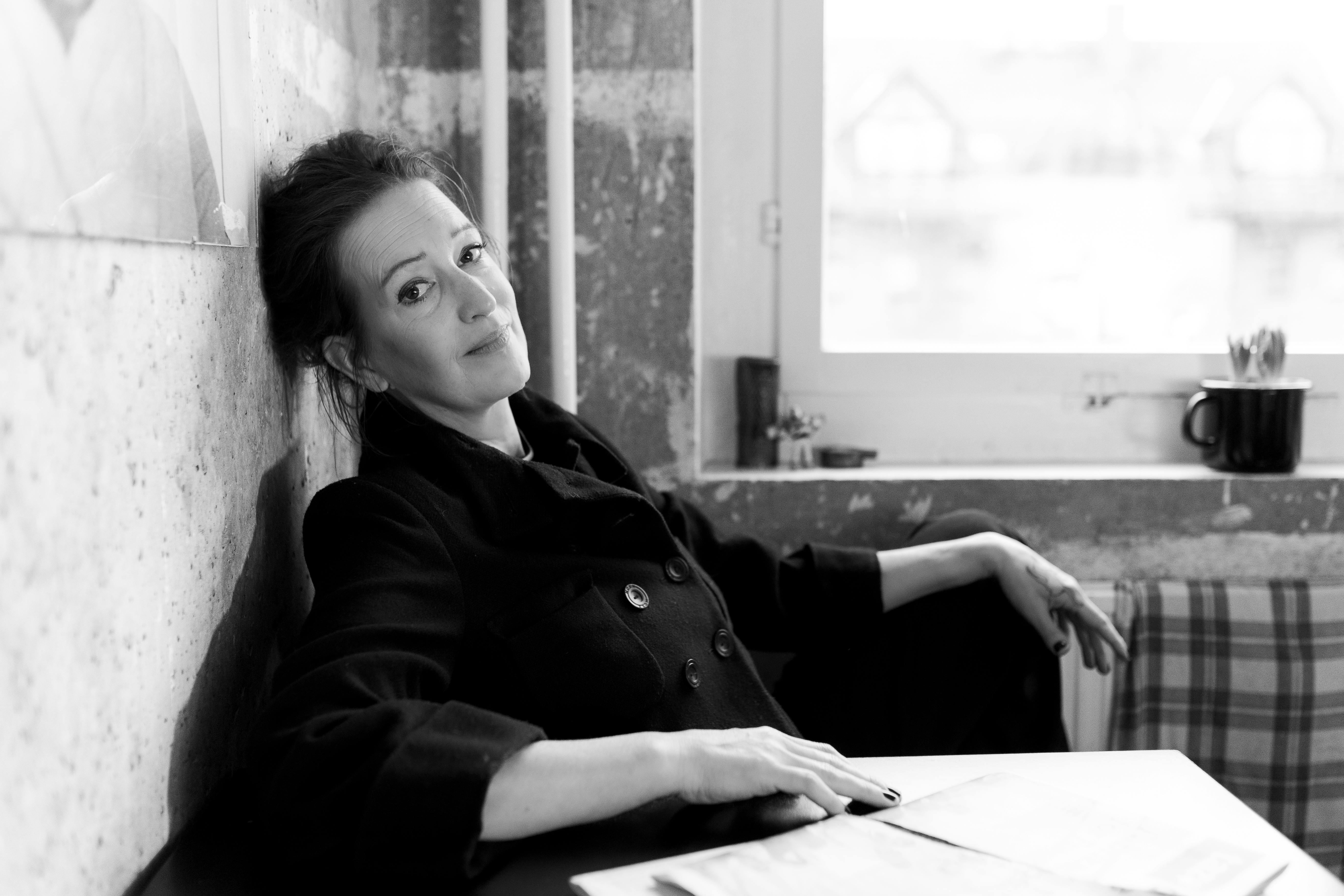 Die Autorin Christine Koschmieder sitzt mit dem Rücken an die Wand gelehnt an einem Tisch.
