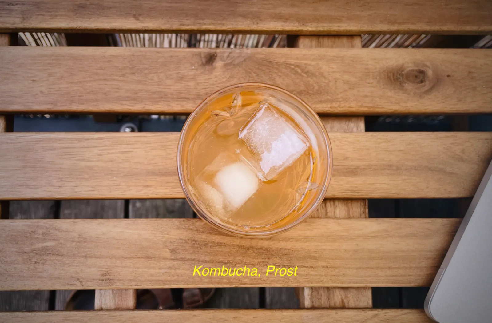 Ein Glas mit Eiswürfeln und Kombucha steht auf einem Balkontisch