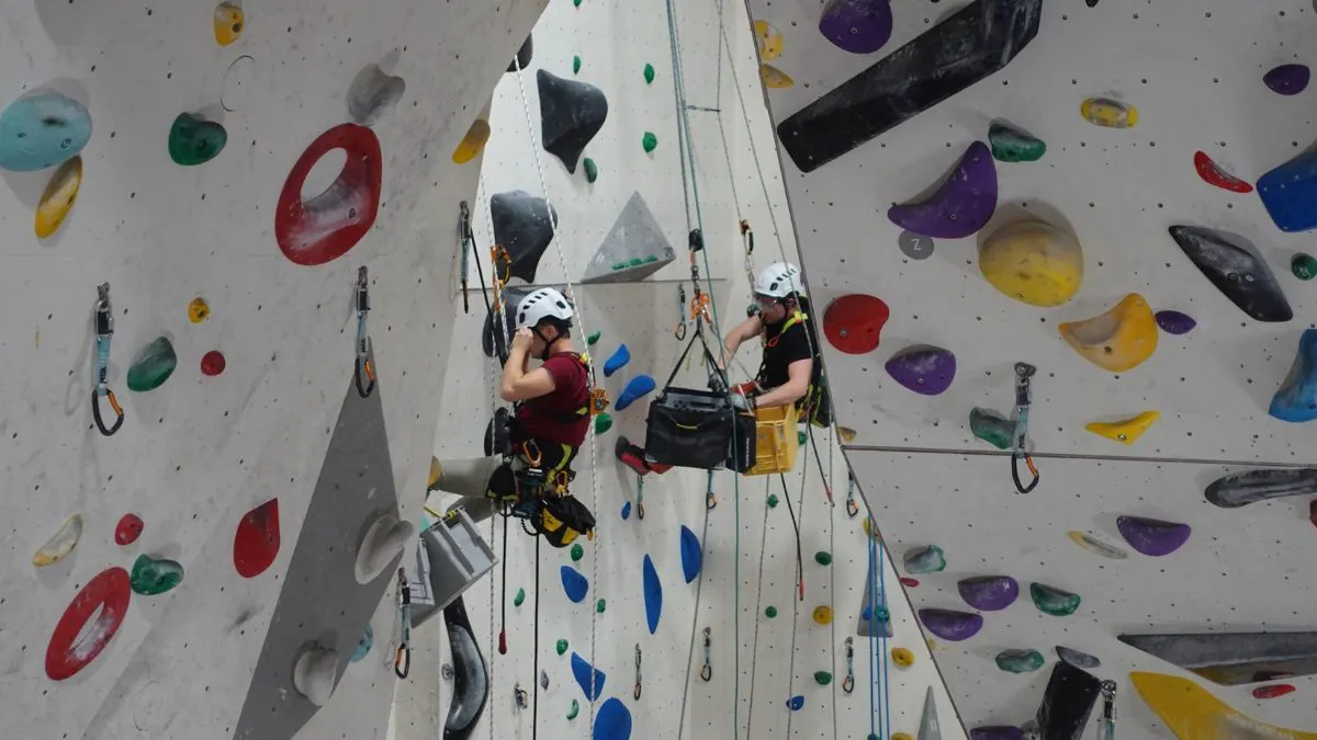 Das Bild zeigt eine Wand in einer Kletterhalle, in der gerade neue Routen geschraubt werden