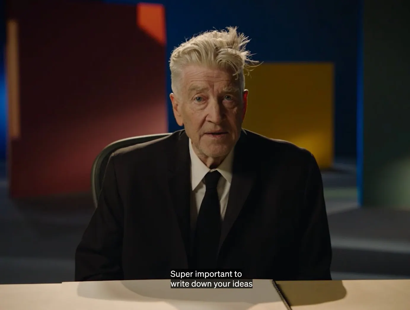 David Lynch im Anzug an einem Schreibtisch. Untertitel: super important to write down your ideas.