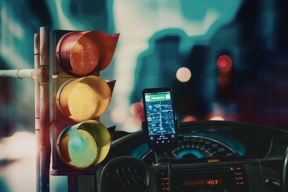 Des feux de signalisation à côté d'une voiture dont le conducteur utilise son téléphone comme GPS.