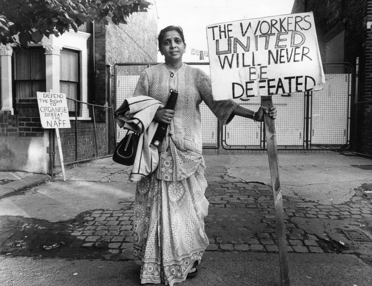 Demonstrantin hält Schild mit Aufschrift: "The Workers united will never be defeated"