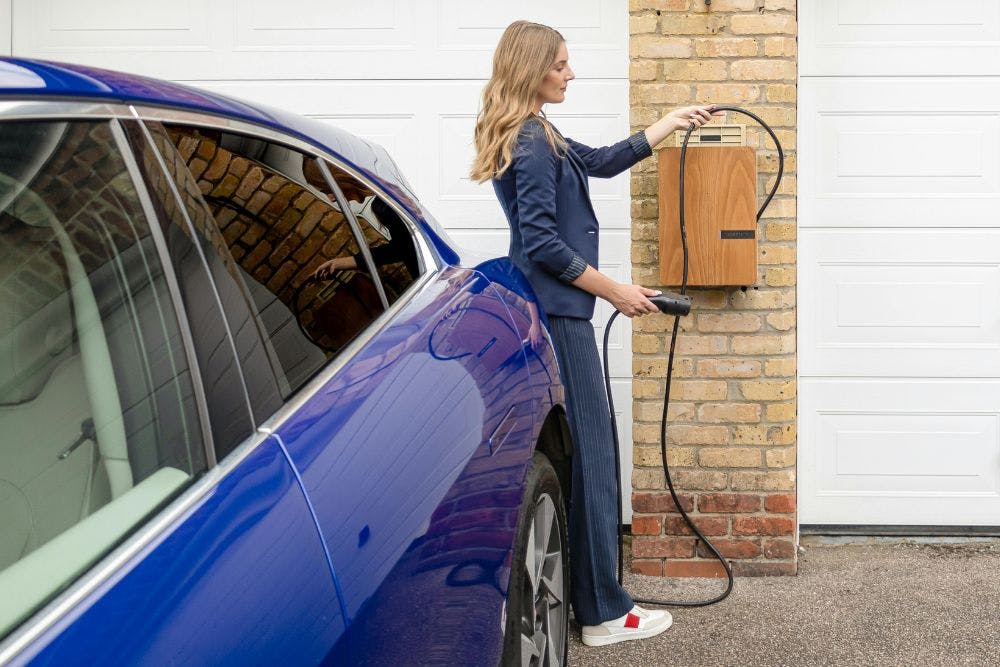 Une femme branche son véhicule électrique à une prise de recharge installée chez elle.
