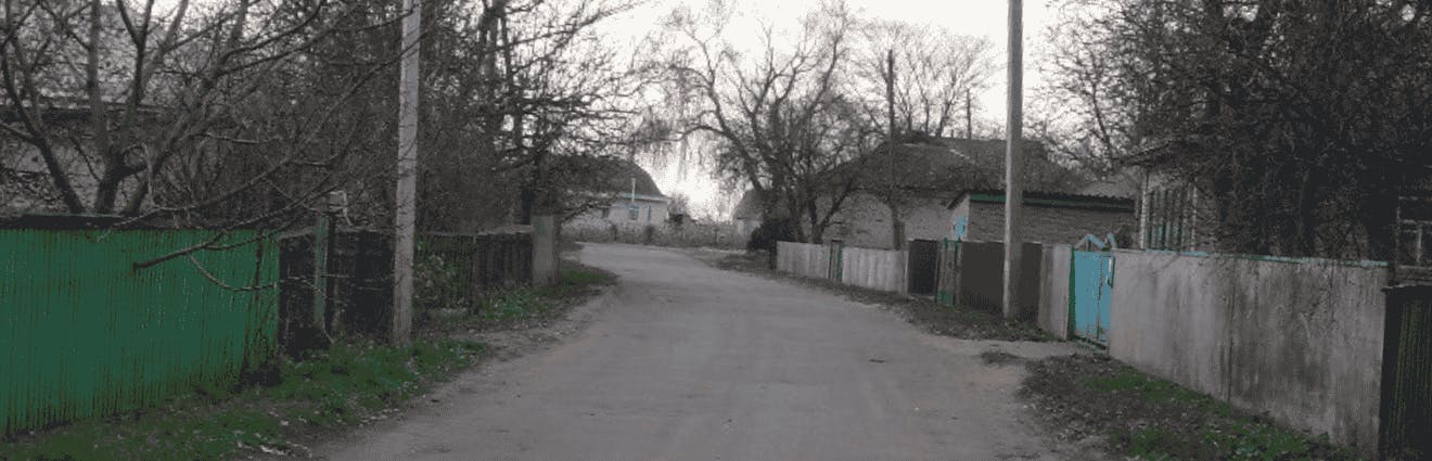 Eine Straße führt auf ein trostlos und verlassen aussehendes Dorf zu.