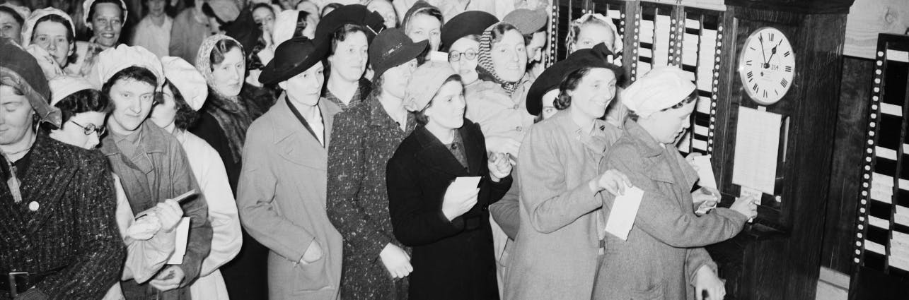 Ein Gruppe von Frauen stempelt sich an der Uhr zur Arbeit ein.