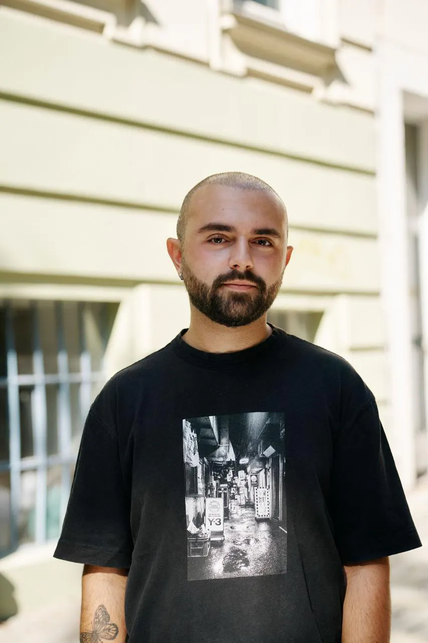 Auf dem Foto ist Dennis Miskić (Freier Journalist) zu sehen. Er trägt ein schwarzes, bedrucktes T-Shirt.