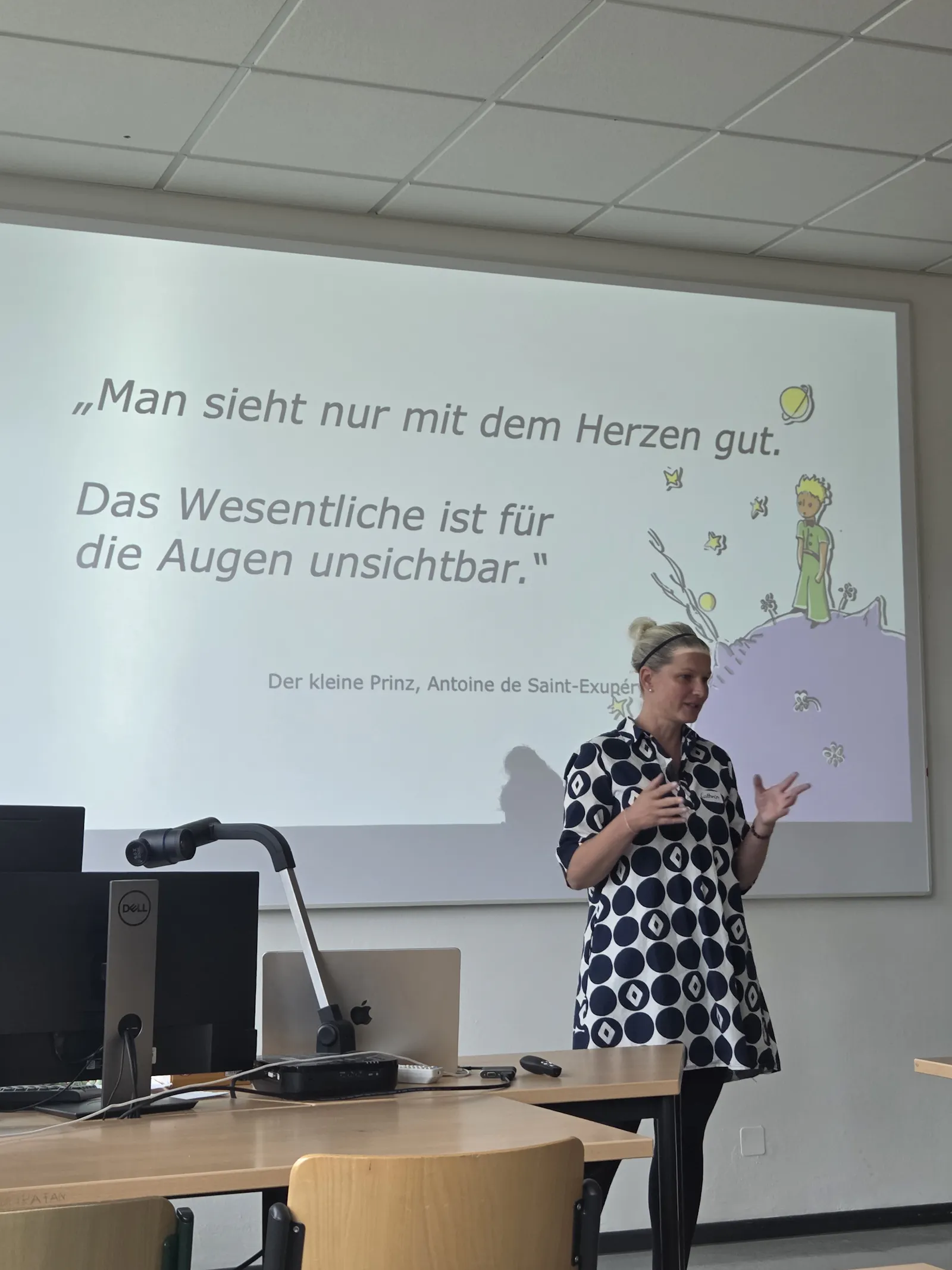 Cathrin Scholz steht vor einem Whiteboard auf dem ein Zitat aus "Der kleine Prinz" steht.