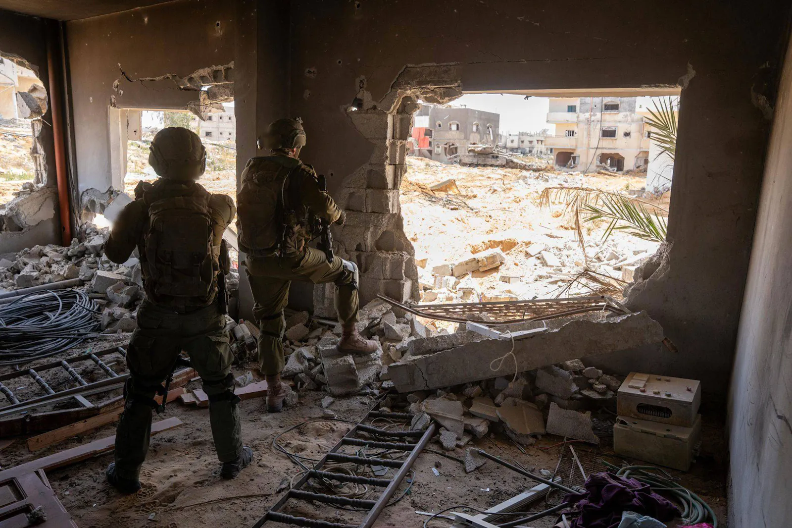 Zwei Soldaten von hinten, in einem zerstörten Haus stehend und die Umgebung beobachtend.