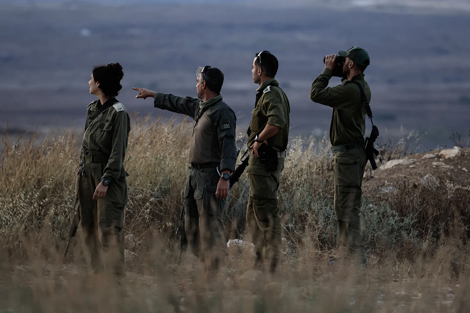 Drei Israelische Soldaten und eine Soldatin ohne Helm beobachten von einem Hügel etwas in der Ferne.