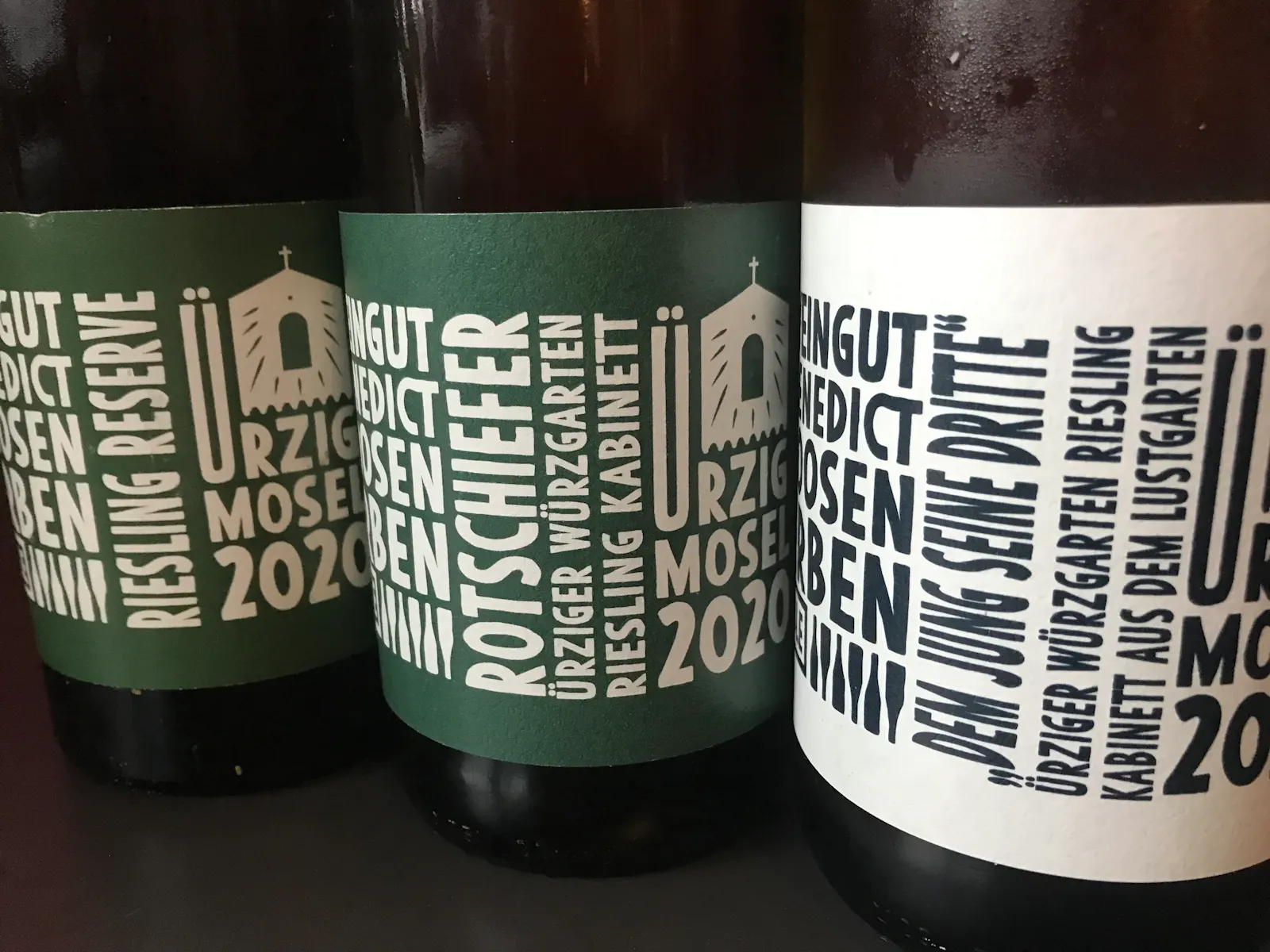Drei Flaschen Riesling des Weinguts Benedict Loosen Erben aus Ürzig an der Mosel stehen auf einem Tisch.