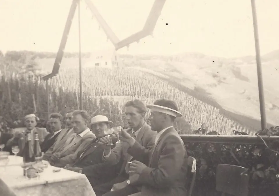 Männer sitzen im Freien an einem Tisch, im Hintergrund sind Weinberge zu sehen