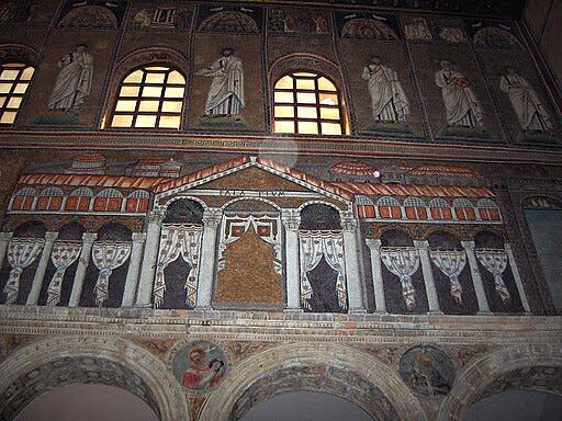 Italiano: Basilica di Sant'Apollinare Nuovo a Ravenna: "Il palazzo di Teodorico". Mosaico di scuola ravennate italo-bizantina, completato entro il 526 d.C. dal cosiddetto "maestro di Sant'Apollinare". Dopo la sconfitta del re goto Teodorico, i mosaici murali del suo palazzo e questi della cattedrale furono rifatti dai bizantini per cancellare ogni traccia dei precedenti dominatori. I dignitari Goti di questo mosaico furono frettolosamente rimpiazzati da tende, probabilmente per mancanza di tempo. Rimangono diverse tracce del mosaico precedente: per esempio un pezzo di un braccio sulla terza colonna da sinistra.