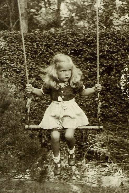 Ein Mädchen mit blonden, langen Haaren sitzt auf einer Schaukel.