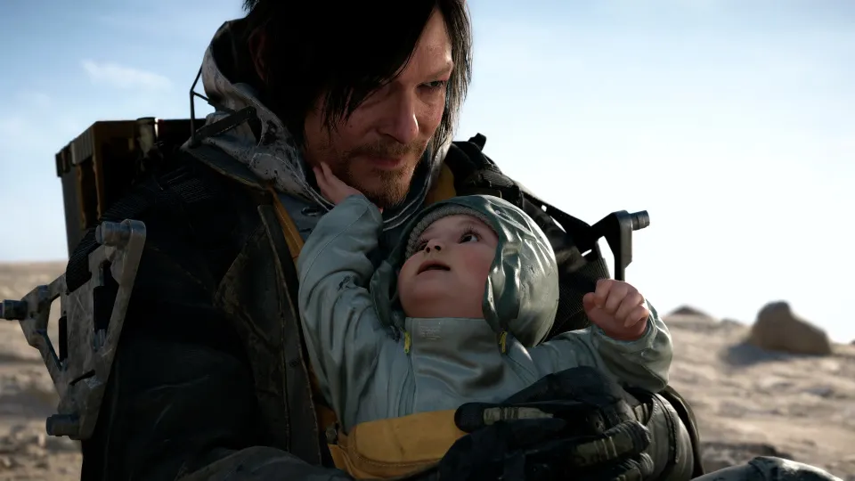Ein Screenshot aus "Death Stranding" zeigt Protagonis Sam und ein Kleinkind in seinem Arm, dass seinen Kopf nach oben reckt um ihn anzuschauen und ihn mit seiner rechten Hand an der Wange berührt
