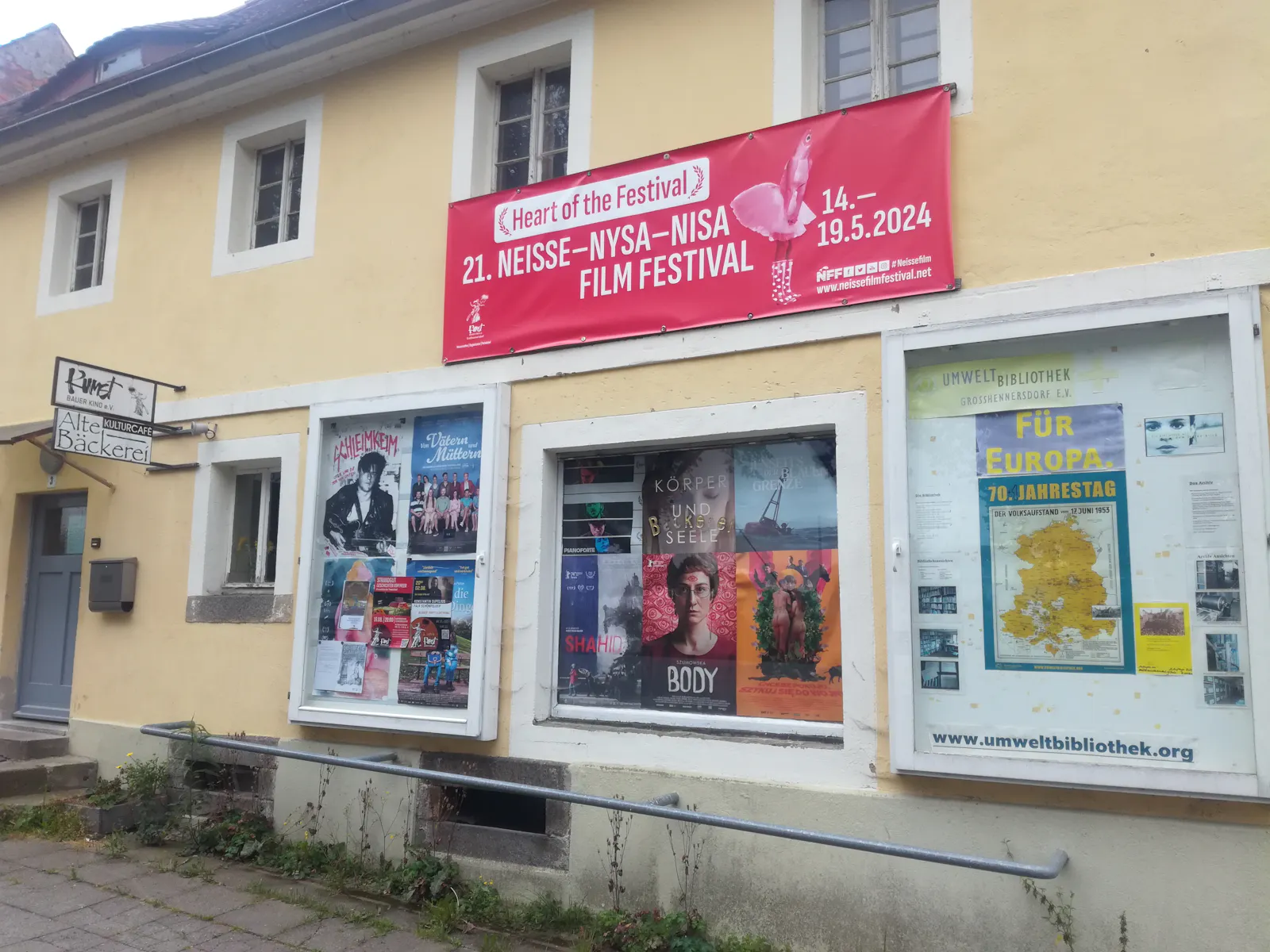 Frontseite der Alten Bäckerei mit Filmplakaten, Schautafel der Umweltbibliothek, Banner des Neiße-Filmfestivals.