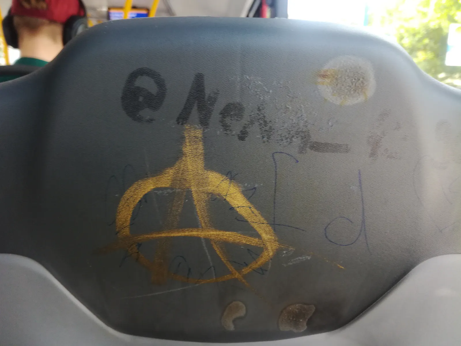 Hintere Seite eines Sitzes im Bus. Anarcho-A (Graffiti), "fd" ergänzt mit Kugelschreiber.