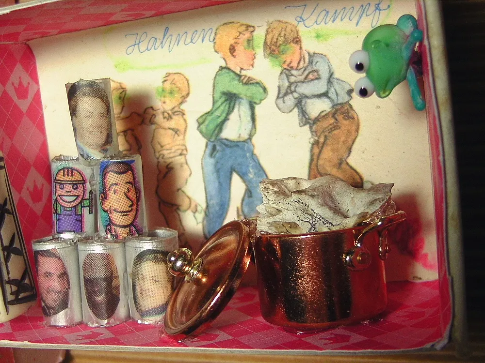 Shadow box "Cockfights" with fighting boys. A bone is cooking in a pot, next to it are canned goods with portraits of men. A glass frog looks doubtful.