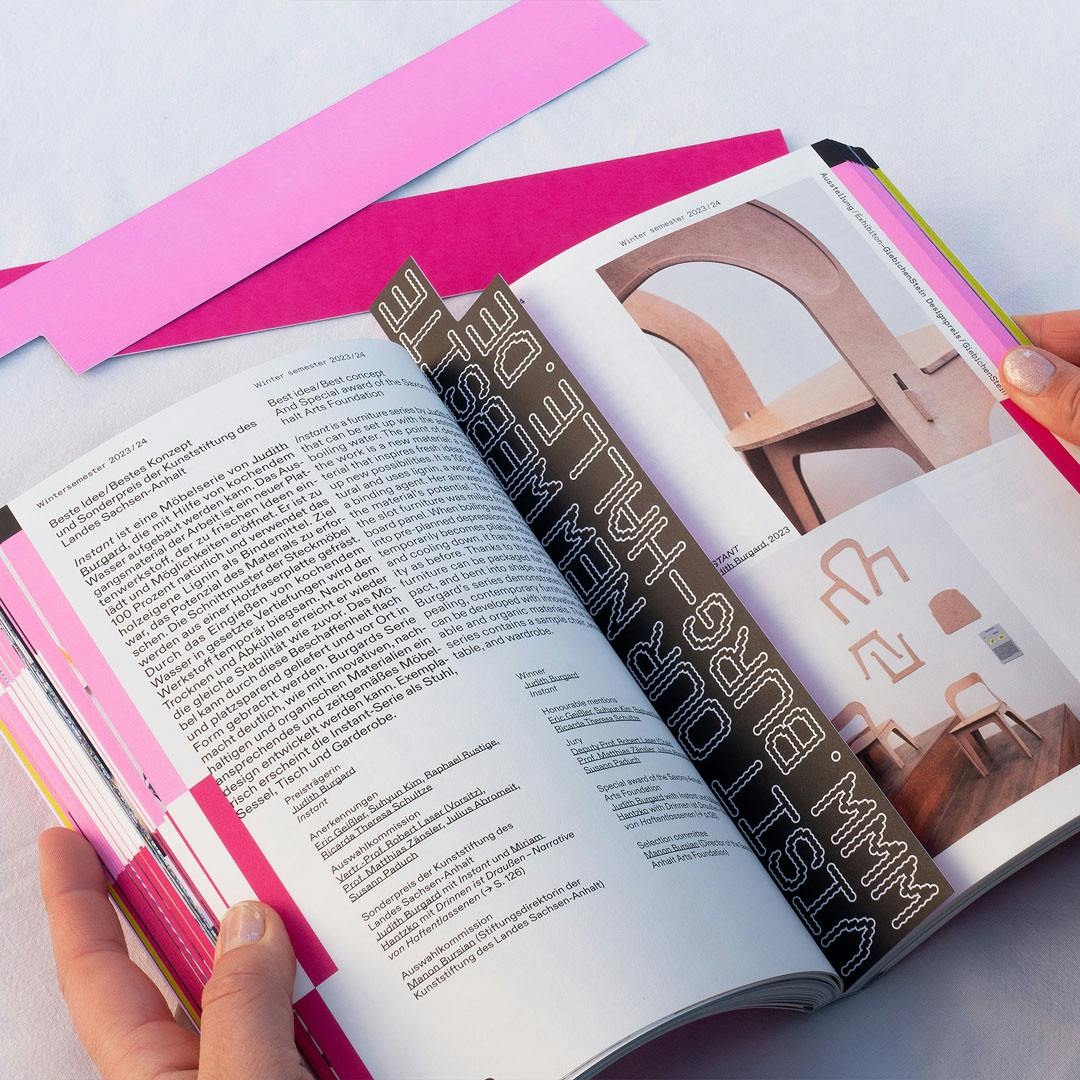 Open book showing text in German and photos of wooden furniture with curved backs and a room interior with chairs and wall decorations
