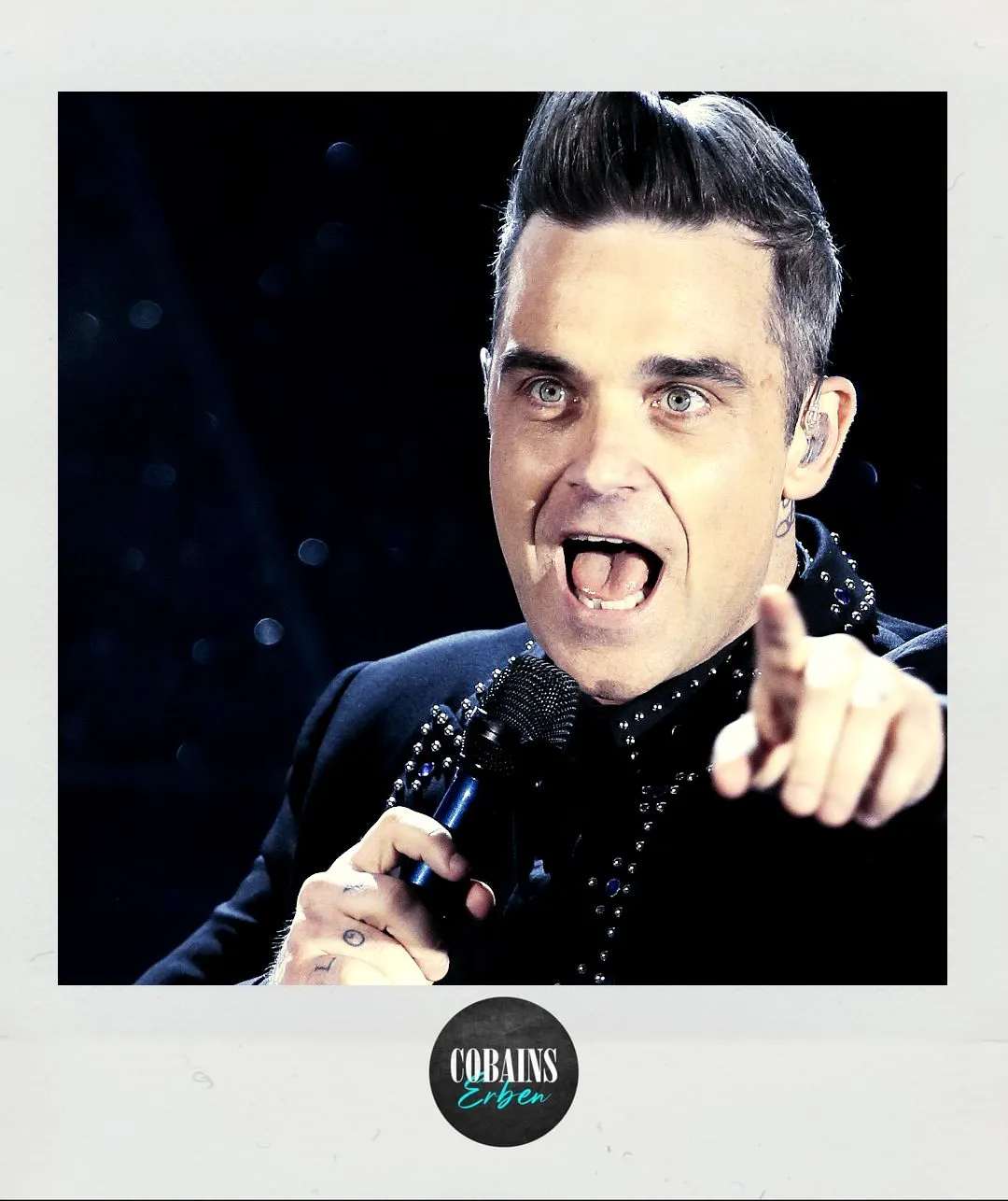 Robbie Williams singt und zeigt mit der linken Hand ins Publikum.