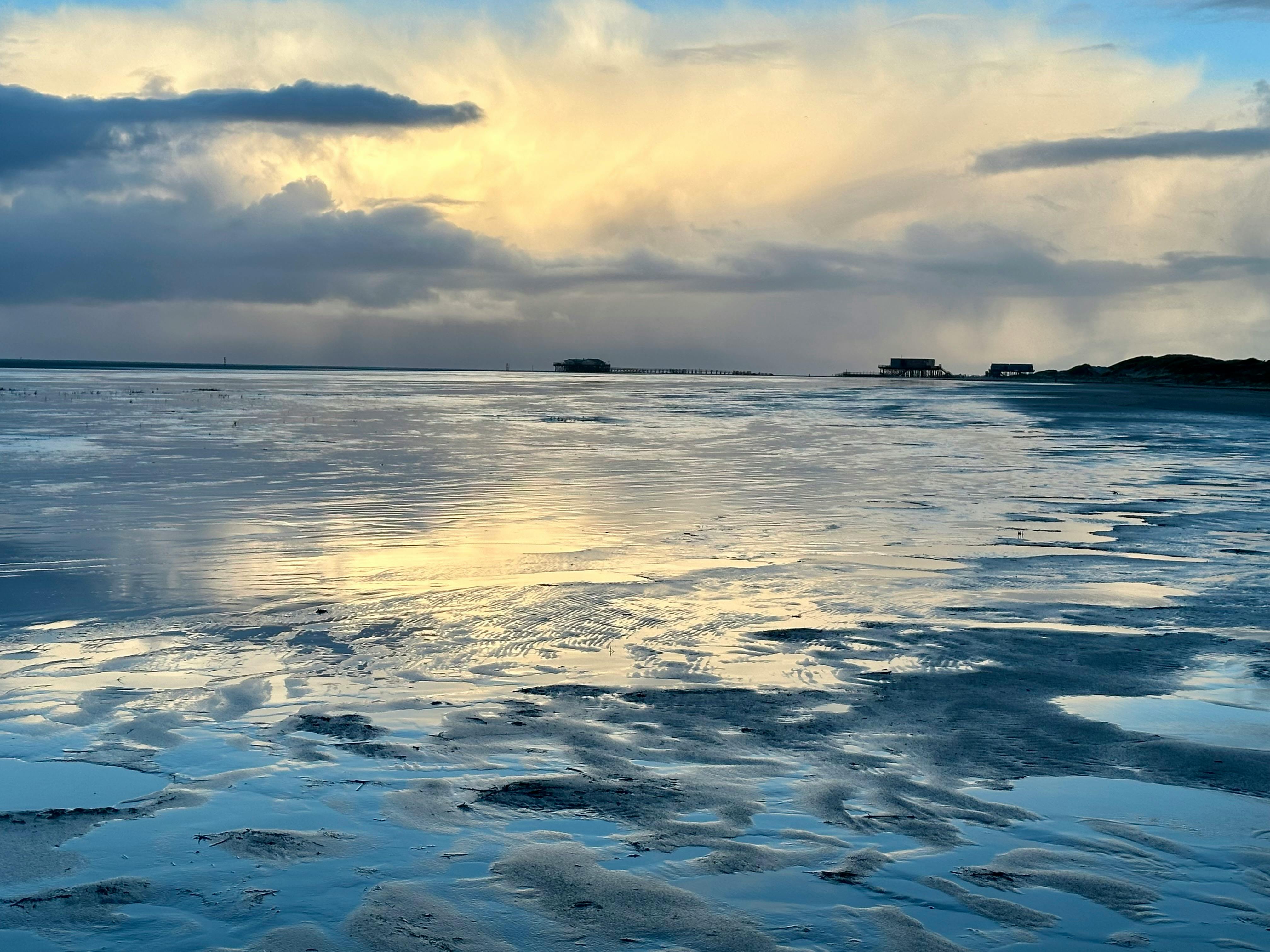 Strand von St- Peter Ording im Winter. Der Strand ist feucht und der dramatische Himmel spiegelt sich dunkelblau darin.