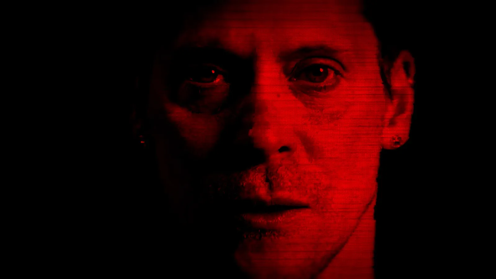Ein Screenshot aus Dead Take. Neil Newbom in der Rolle von Chase ist in rotes Licht getaucht und blickt in die Kamera.