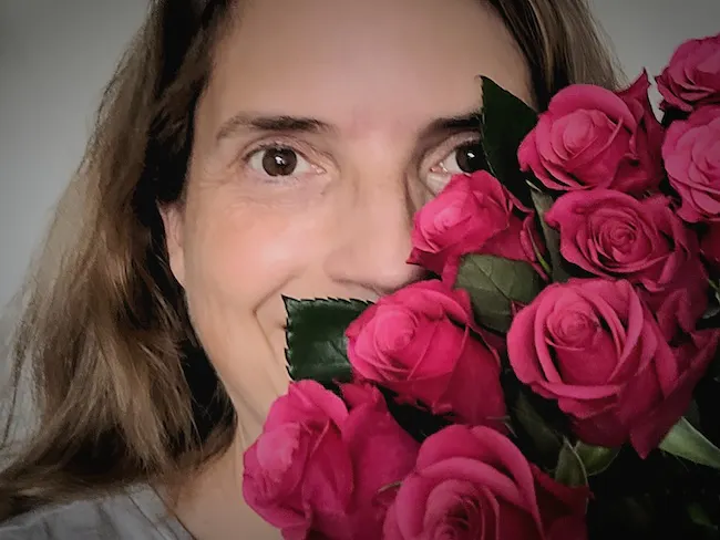 Christine Piontek mit einem Strauß mauvefarbener Rosen, der ihr Gesicht halb verdeckt.