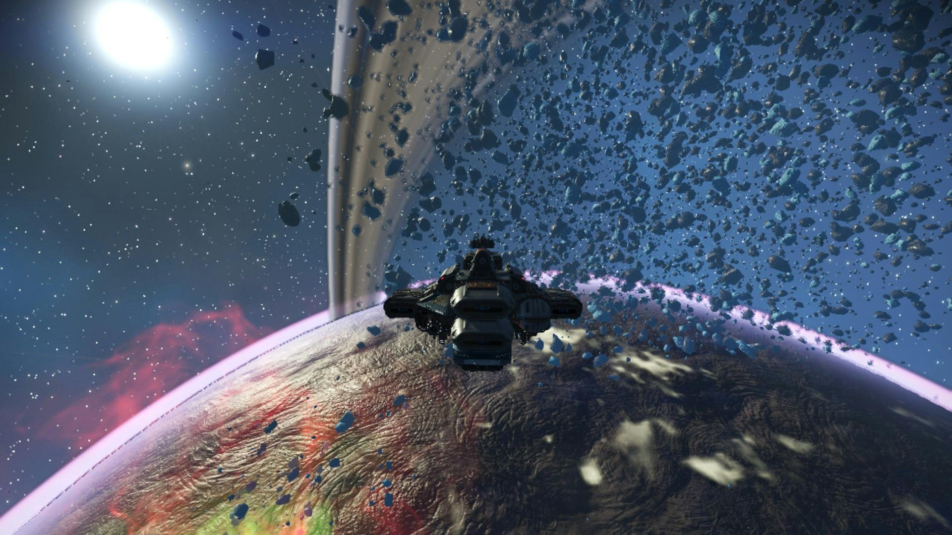 Ein Asteroidengürtel in No Man's Sky um einen Planeten, der von roten Gasen umgeben ist, im Hintergrund leuchtet eine Sonne.