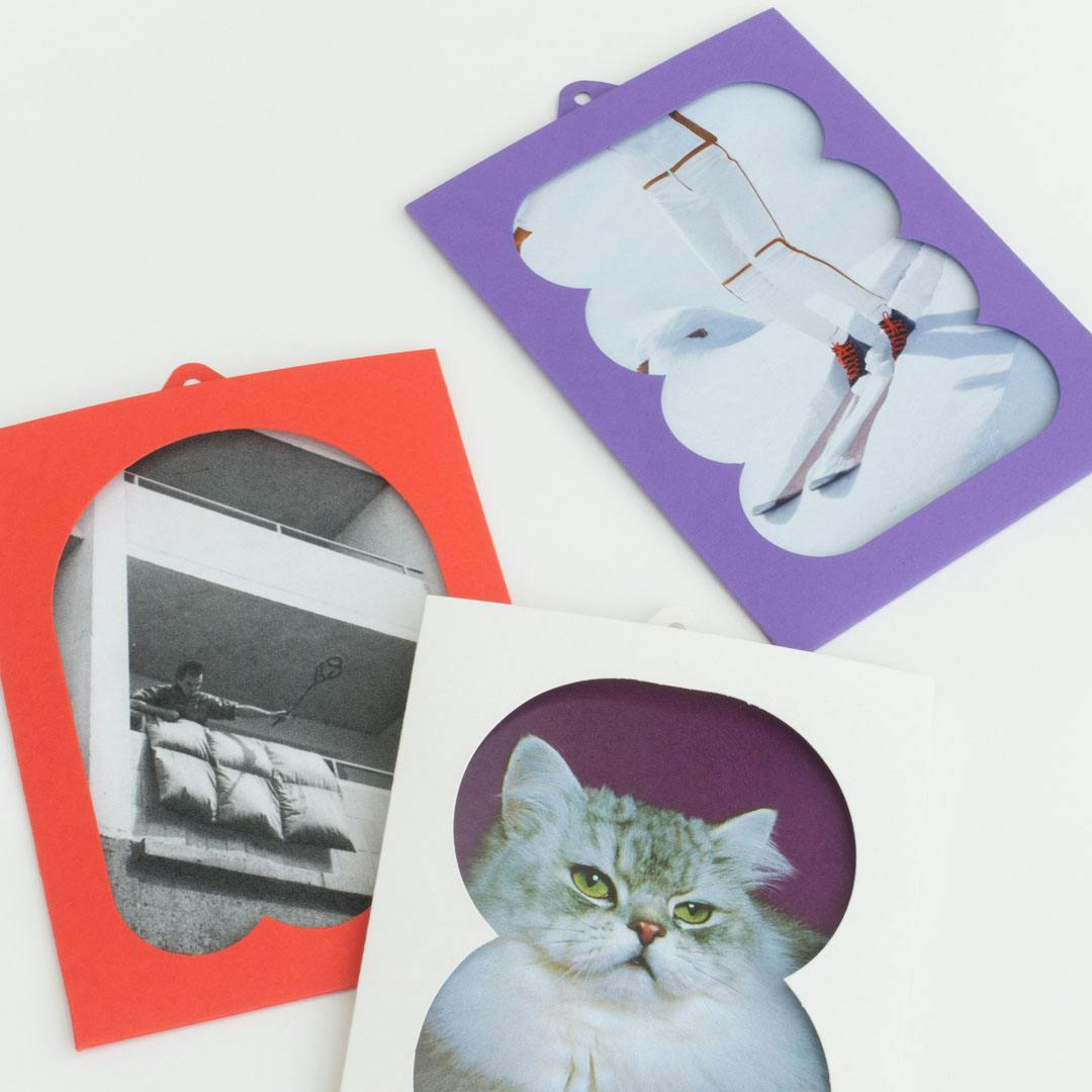 Paper frames in red and purple with cut-out shapes showing black-and-white and color photographs including a cat, a person, and legs on skiers