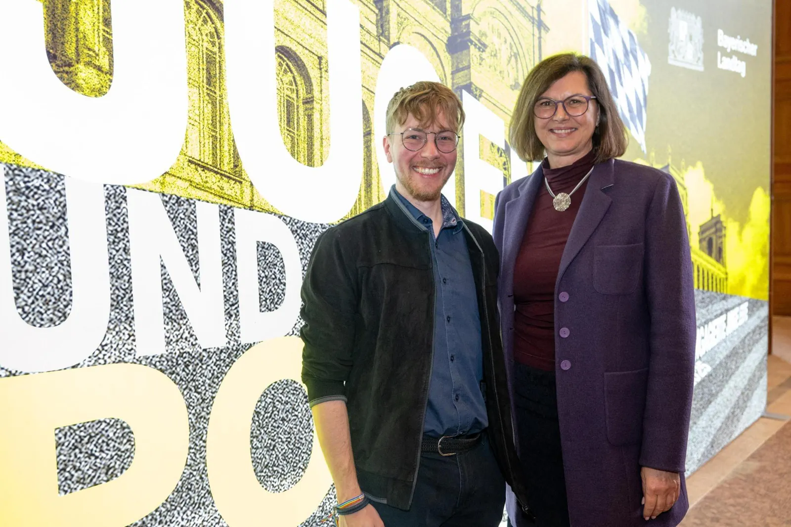 Thomas Laschyk und Ilse Aigner vor einer Fotowand des bayerischen Landtages