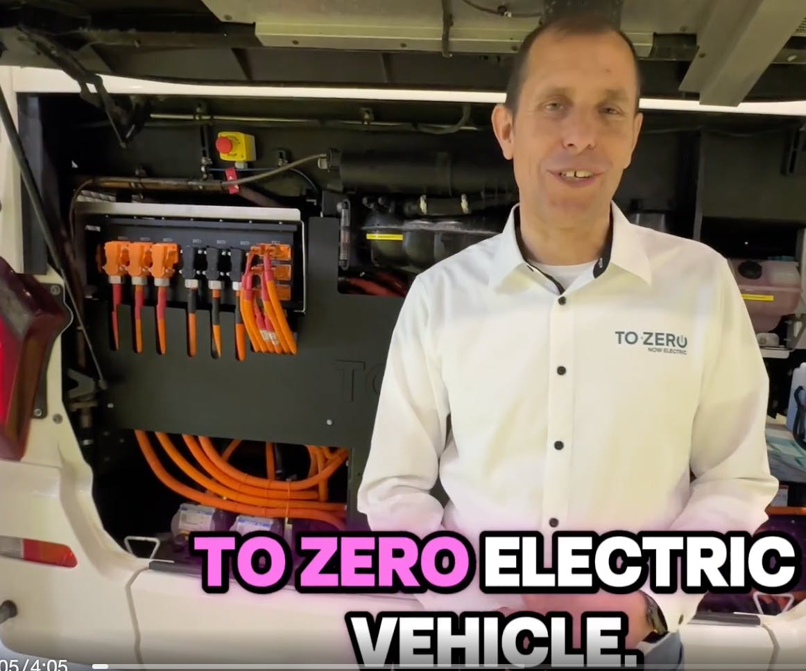 Ein Mann mit weißem Hemd steht vor einem geöffneten elektrischen Motor eines Busses.