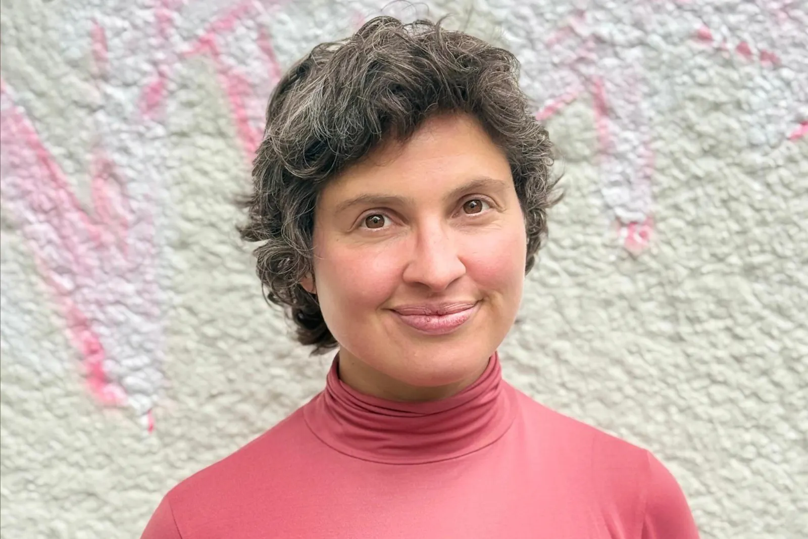Lara Newiger trägt ein pink-rotes Oberteil und steht vor einer weißen Wand