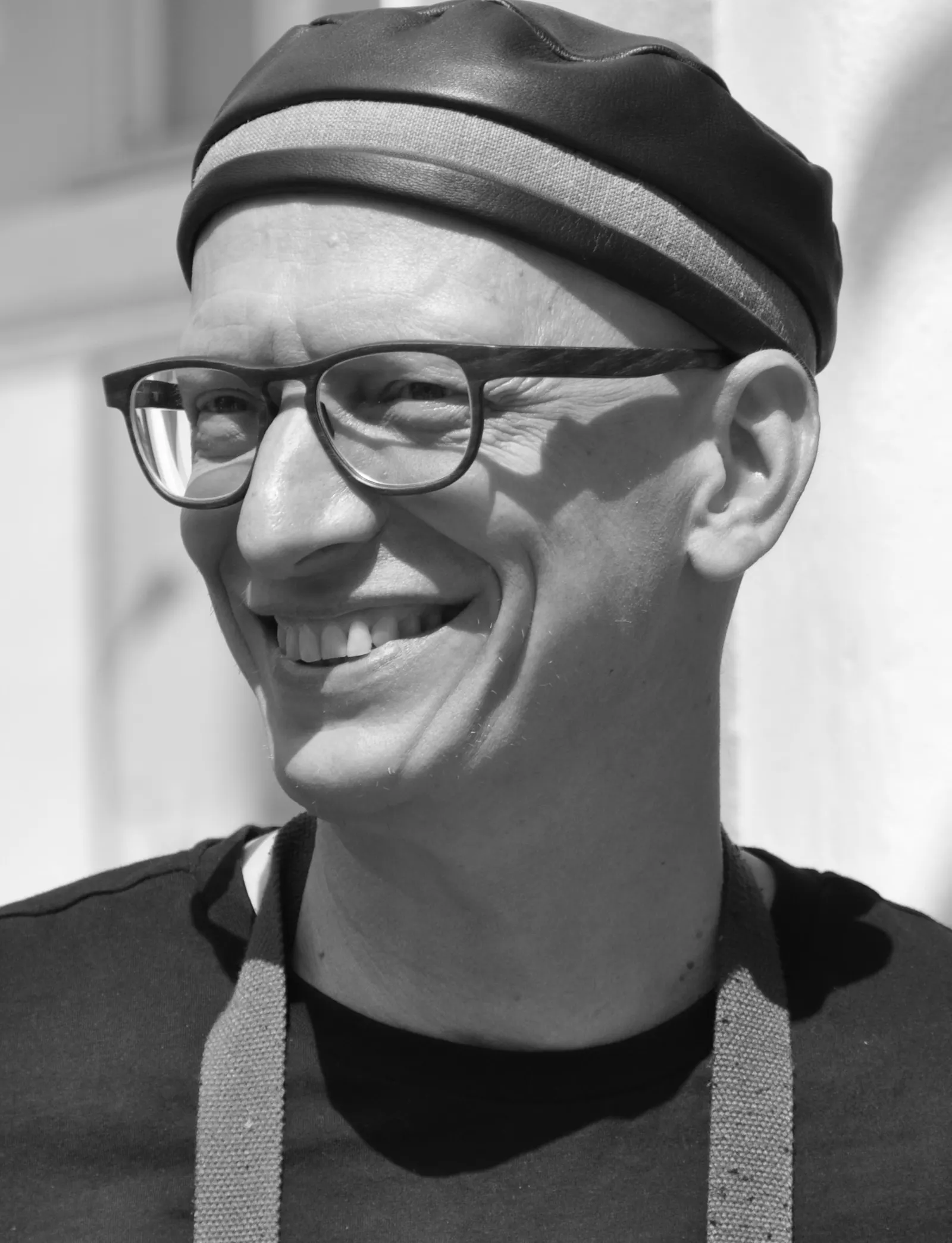 Ein Mann mit Brille und einer Ledermütze lacht.