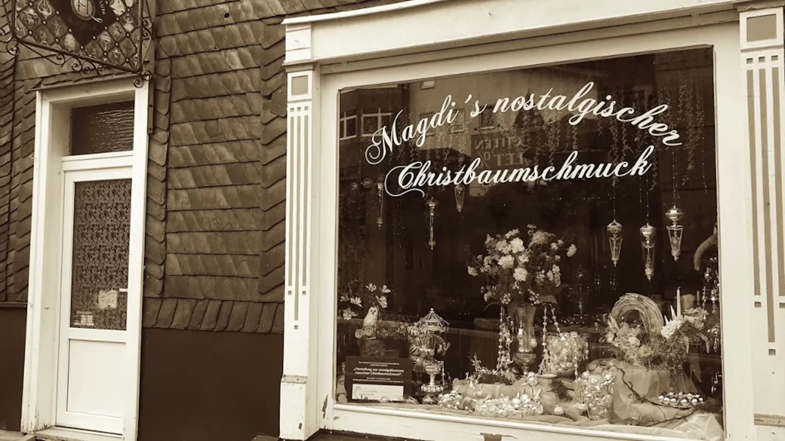 Frontansicht eines Geschäfts. Links eine Tür, rechts ein fast bodentiefes großes Schaufenster mit der Aufschrift "Magdi's Nostalgischer Christbaumschmuck". Silberne Weihnachtskugeln in der Auslage