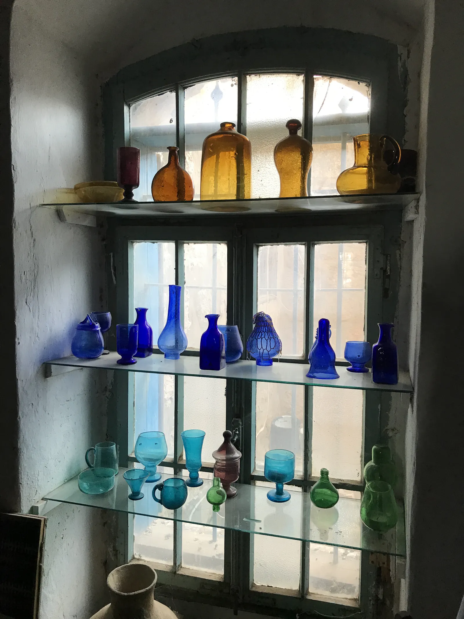 Flaschen verschiedenfarbig, karamellig, blau, türkis, grün in einem Fensterregal