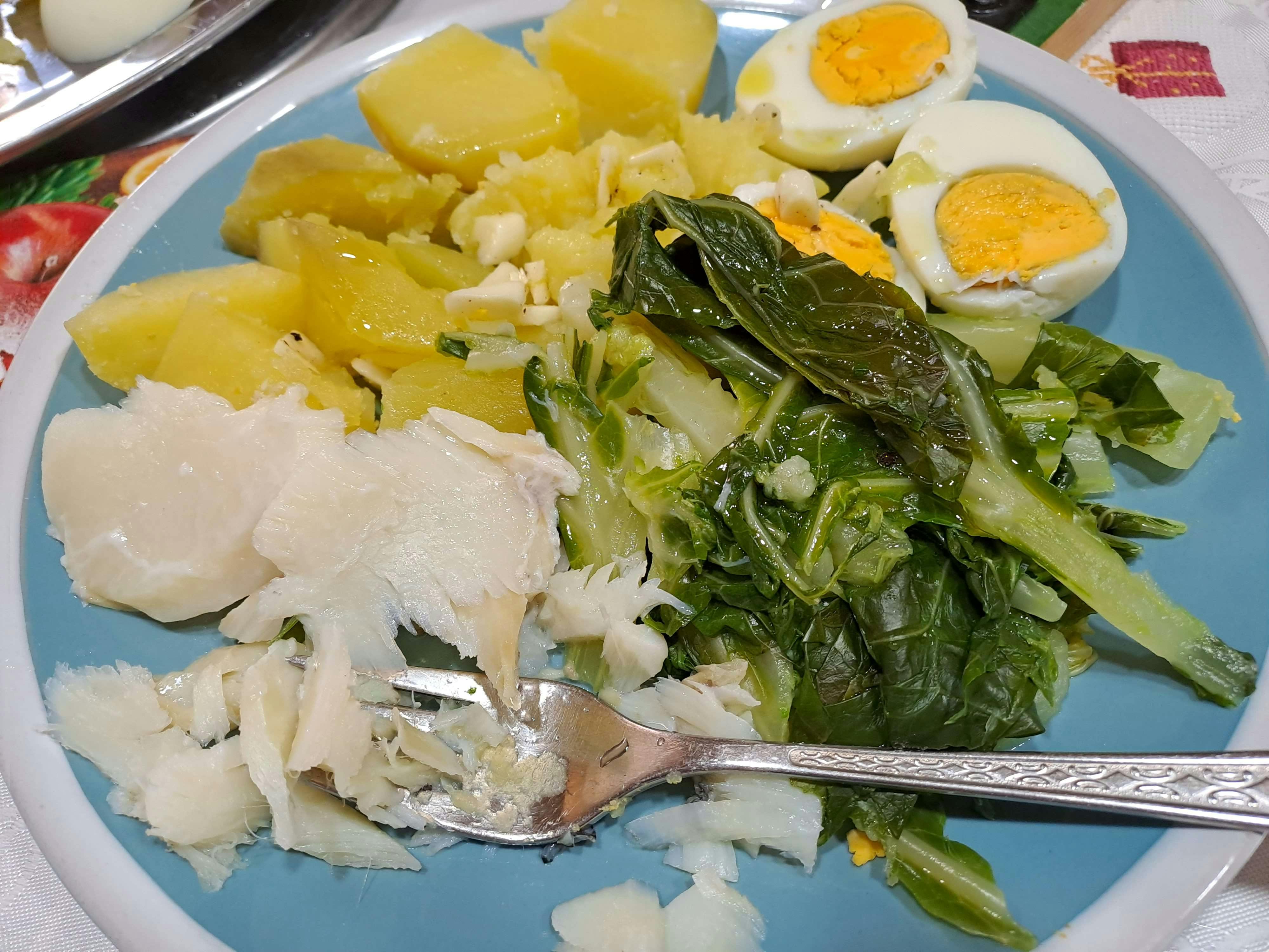 Blauer Teller mit einem Gericht aus Salzkartoffeln, hartgekochten Eiern, Kohl und zerpflücktem weißen Fisch.