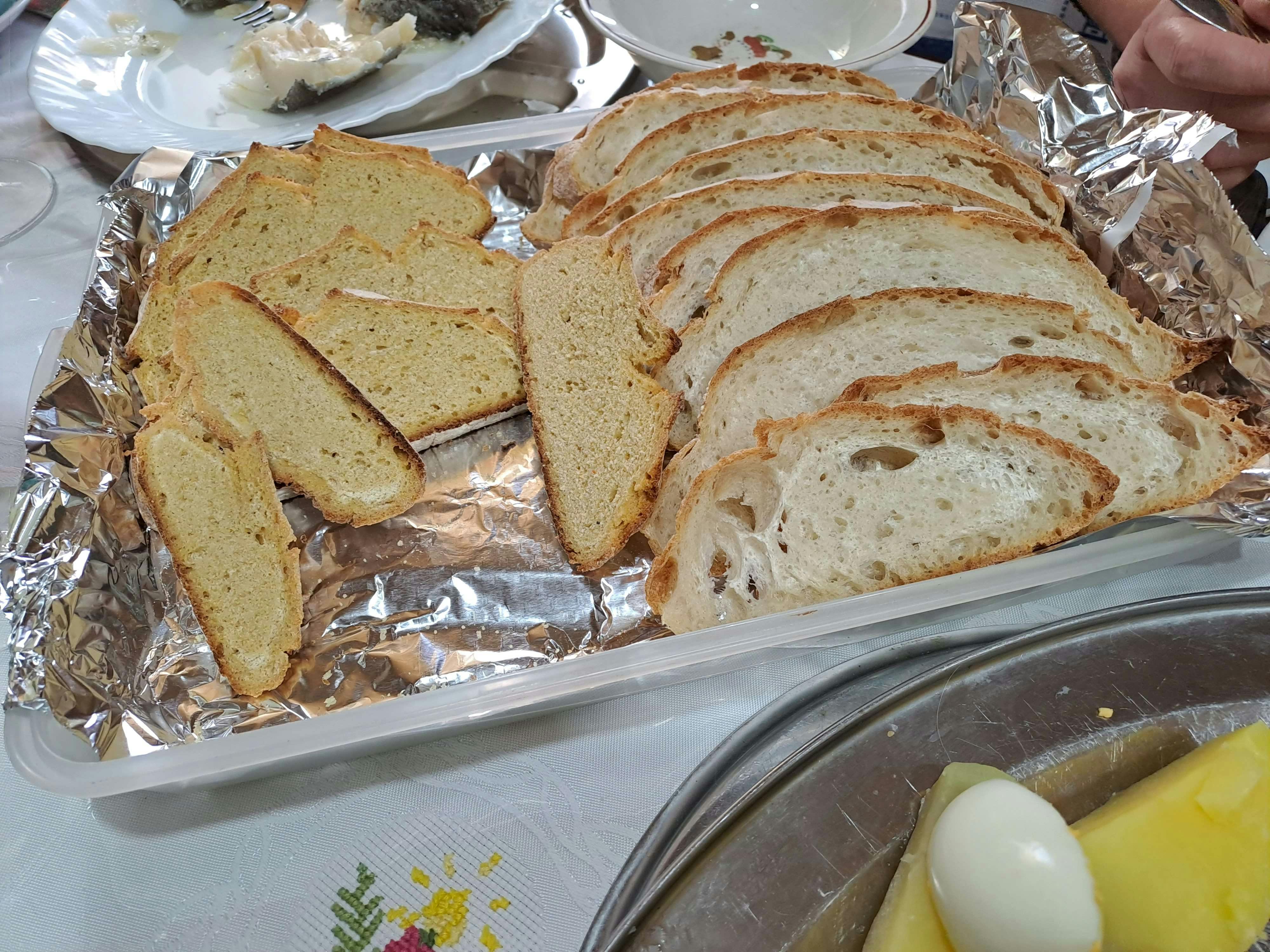 Aufgeschnittenes portugiesisches Brot und helles Gebäck in Scheiben, auf Alufolie in einer Kunststoffbox angerichtet.