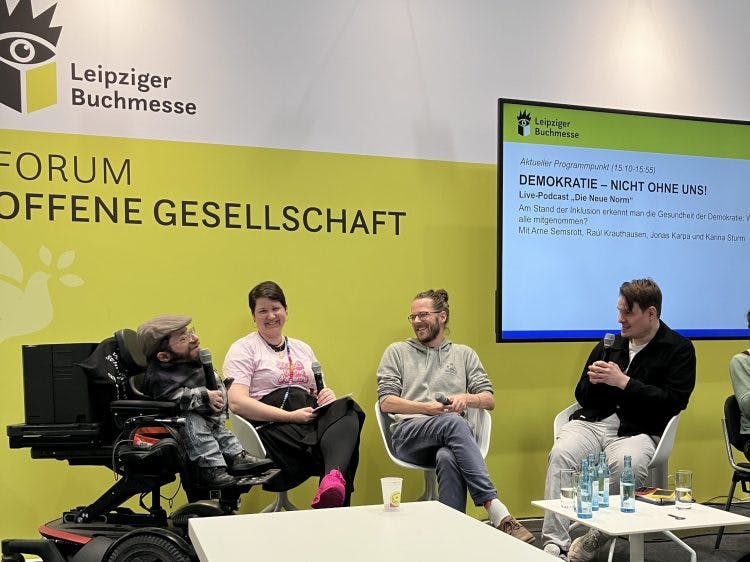 Raúl Krauthausen, Karina Sturm, Arne Semsrott und Jonas Karpa sitzen auf einer Bühne der Leipziger Buchmesse und halten Mikrofone in der Hand.